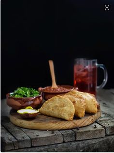 some food is sitting on a wooden board next to a glass of tea and a cup