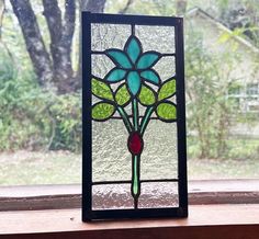 a stained glass flower sitting on top of a window sill in front of a tree