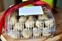 a plastic container filled with cookies on top of a wooden table next to a red ribbon