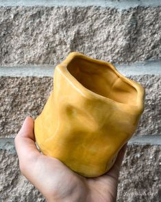 a hand holding a yellow vase in front of a brick wall