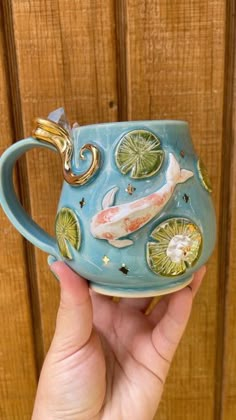 a hand holding a ceramic mug with fish and lily pads on it's side