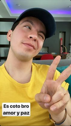 a man in a yellow shirt and black hat making the peace sign with his fingers