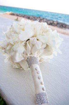 a bridal bouquet sitting on top of a white table next to the ocean and beach