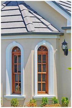 two windows on the side of a white building with blue roof and red shutters