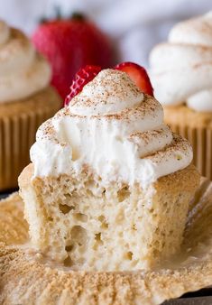 a close up of a cupcake with whipped cream and strawberries in the background