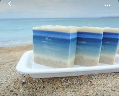 three bars of soap sitting on top of a white plate next to the ocean and sand