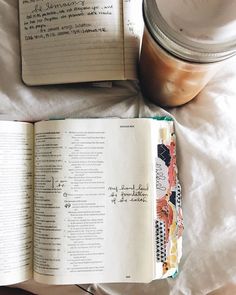 an open book sitting on top of a bed next to a jar of liquid and spoon