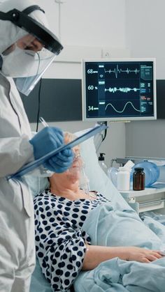 a person in a hospital bed with an oxygen mask on and another wearing a protective suit