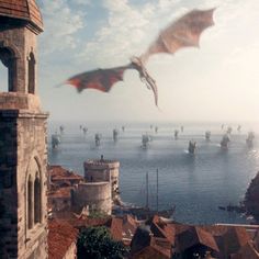 a large dragon flying over a city next to the ocean