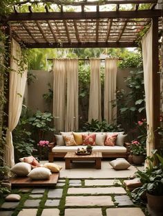 an outdoor living area with couches, pillows and plants on the ground in front of a pergolated wall