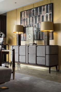 a living room with two lamps and a large painting on the wall above it's sideboard