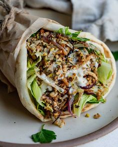 a pita sandwich on a plate with lettuce and other ingredients around it