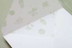 two envelopes with white paper and green leaves on the inside one is folded in half