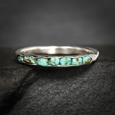 a silver ring with turquoise stones on it sitting on top of a black stone surface