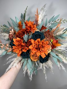 an arrangement of flowers and feathers is being held by a person's hand on a gray background