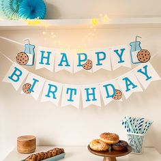 a happy birthday banner with cookies and donuts hanging from it's side on a table