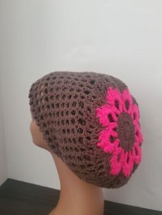 a crocheted hat with pink and brown flowers on the front, sitting on a mannequin head