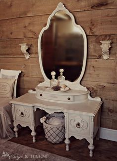 an antique white vanity and mirror in a room with wood paneling on the walls