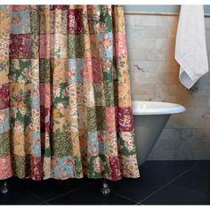 a bath tub sitting next to a shower curtain covered in colorful patchwork cloths