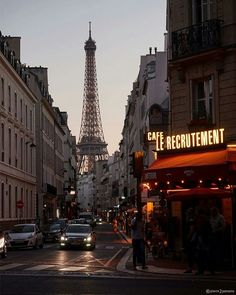 the eiffel tower is lit up at night in front of some buildings and cars