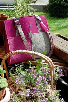 two purses sitting on top of a wooden bench next to flowers and plants in pots