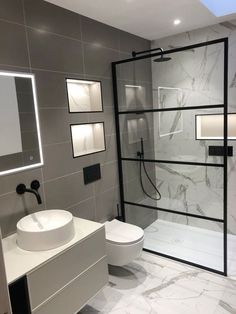 a bathroom with a glass shower door, toilet and sink in white marbled tile