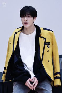 a young man sitting on top of a chair wearing a yellow jacket and white t - shirt