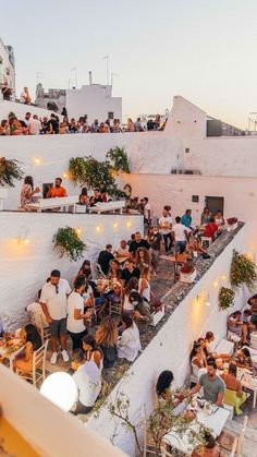 many people are sitting at tables and eating outside in an outdoor dining area with white walls