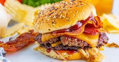 a bacon cheeseburger with lettuce, tomato and onion on the side