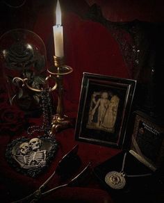 a table topped with pictures and a lit candle next to a framed skeleton on a red cloth