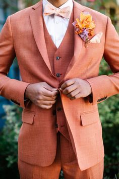 a man in an orange suit and flower boutonniere is holding his bow tie