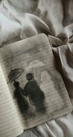 an open notebook with a drawing of two people holding umbrellas on top of a bed