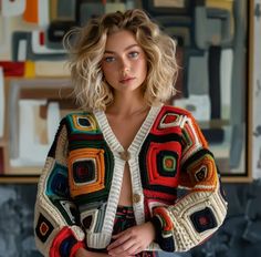 a woman standing in front of a painting wearing a multicolored crocheted cardigan