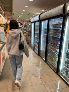 a woman is walking down the aisle in front of refrigerators filled with drinks and beverages