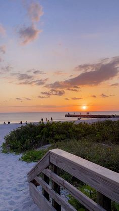 a bench sitting on top of a sandy beach next to the ocean with people in the distance