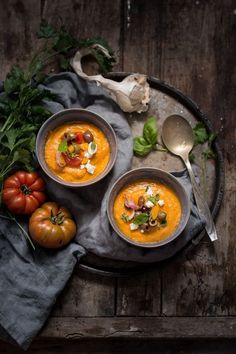 two bowls filled with soup on top of a table next to tomatoes and parsley