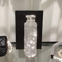 a bottle with some lights on it sitting next to a purse and other items in front of a white curtain