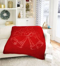 a red knitted christmas blanket on top of a white couch in a living room