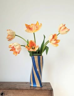 a blue and white striped vase filled with orange flowers on top of a wooden table