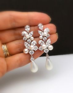 a pair of white pearl and crystal earrings in the palm of someone's hand