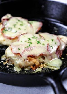 two pieces of meat in a skillet covered in cheese and sauce with parsley