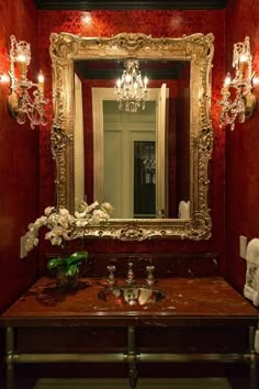 a fancy bathroom with red walls and gold framed mirror above the sink, along with candles