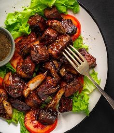 a white plate topped with meat and lettuce next to a bowl of sauce