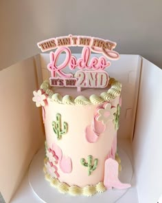 a birthday cake with pink frosting and cactus decorations on top, in a box