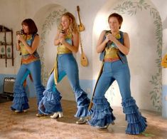 three women in blue and gold outfits are dancing with musical instruments on the floor,