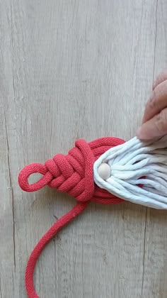 someone is tying a red and white rope on a wooden surface with their hand holding the string