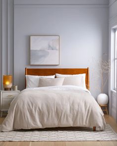 a bed with white linens and pillows in a light blue room next to a window