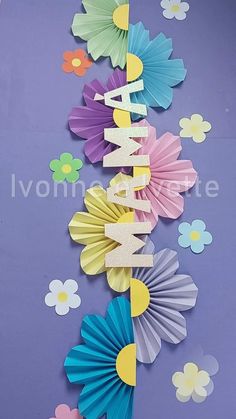 colorful paper fans with the word happy on them are hanging from a purple wall in front of flowers