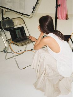 a woman sitting in front of a laptop computer on top of a white table next to a chair