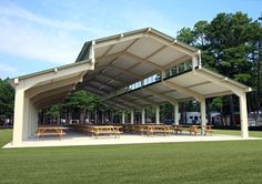 an outdoor pavilion with picnic tables in the foreground and trees in the back ground